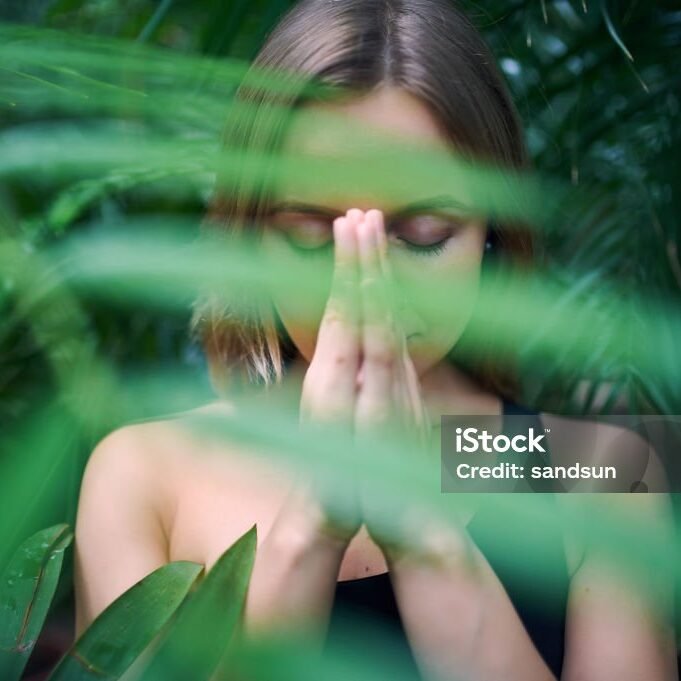 Portrait of cute young woman meditating and doing namaste hand in jungle. Sunny day.